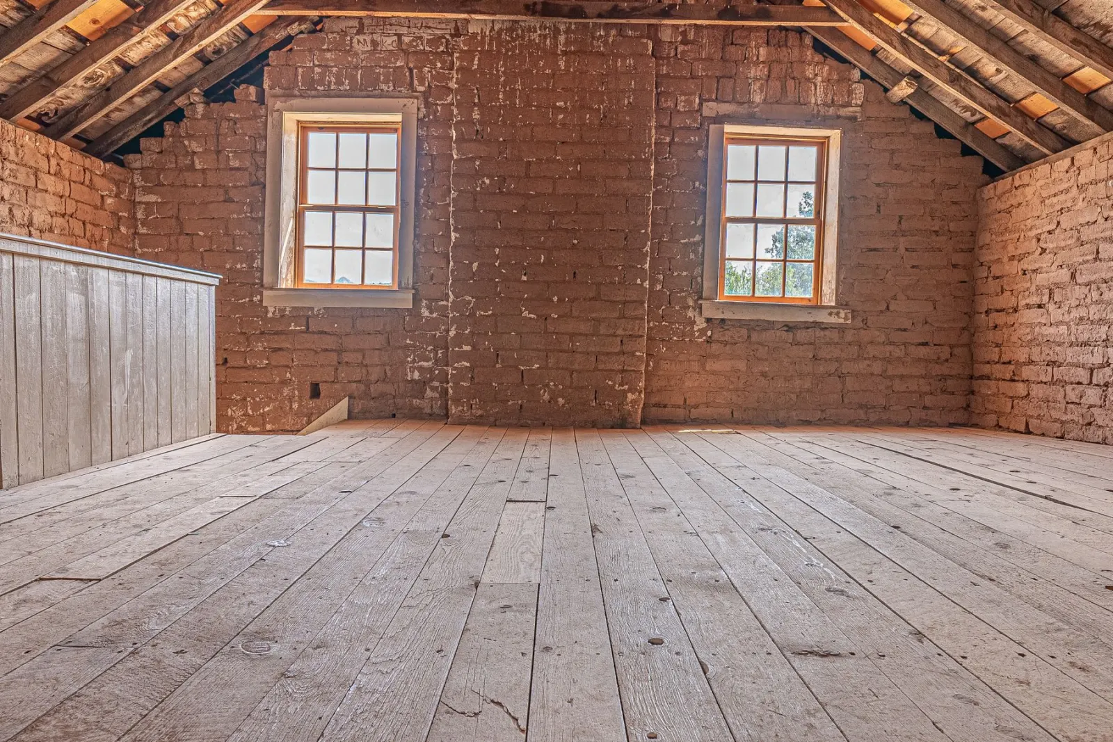 A boarded attic room with exposed brick and a timber floor